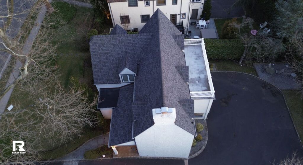 Aerial view of a house with a dark roof and white exterior, beside a curved driveway and trees.