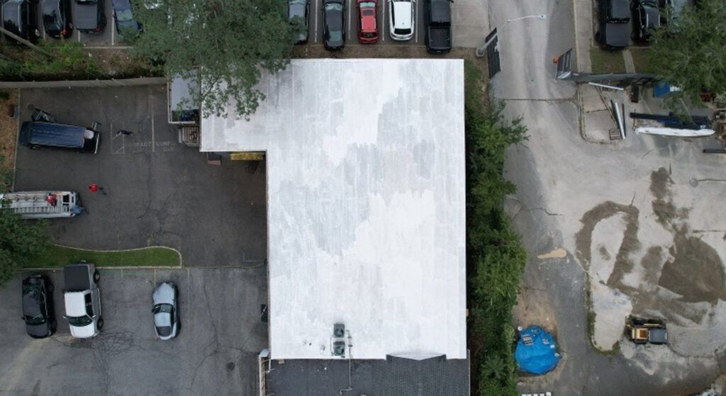 Aerial view of a white-roofed building with parked cars and a dirt lot beside it.