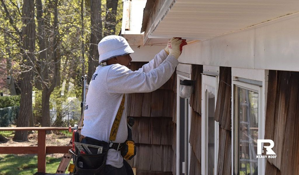 Worker painting white house trim beside windows outdoors