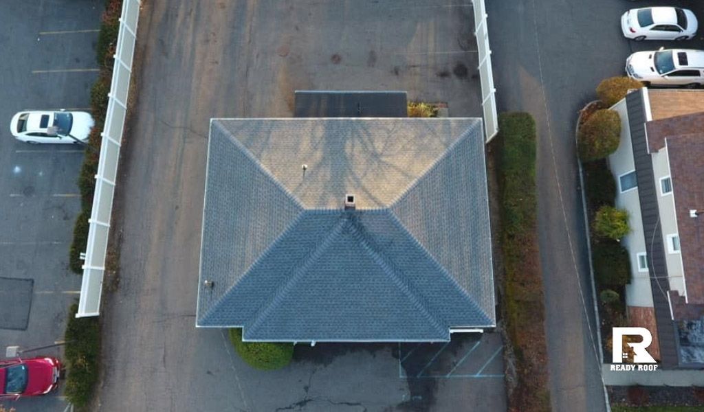 Aerial view of a gray-roofed house with parked cars along a residential street.