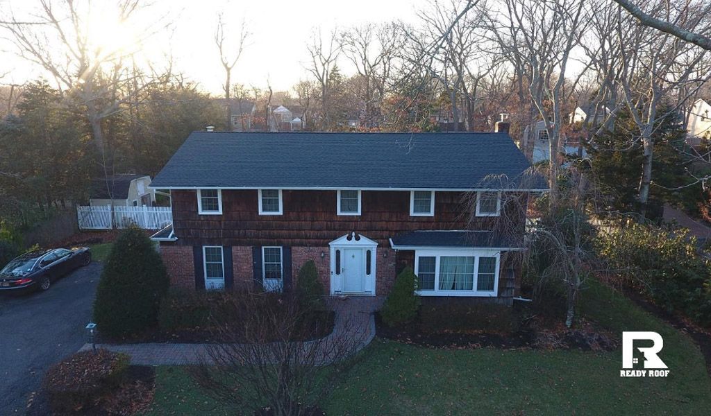Brick two-story house with white trim and blue roof, seen from the front amid trees at dusk