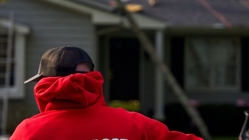 Person in a red hoodie seen from behind in a yard outside a house.