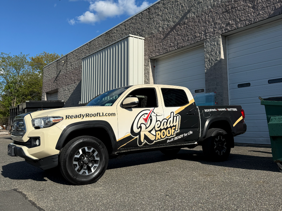 Black-and-white pickup truck with “Deadly Roofs” branding parked beside a building and garage doors