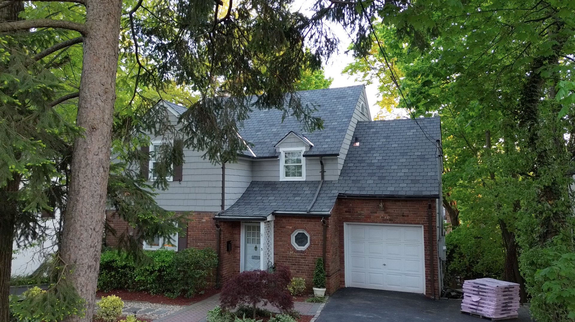 Two-story house with brick and gray siding, white garage, and trees in the front yard