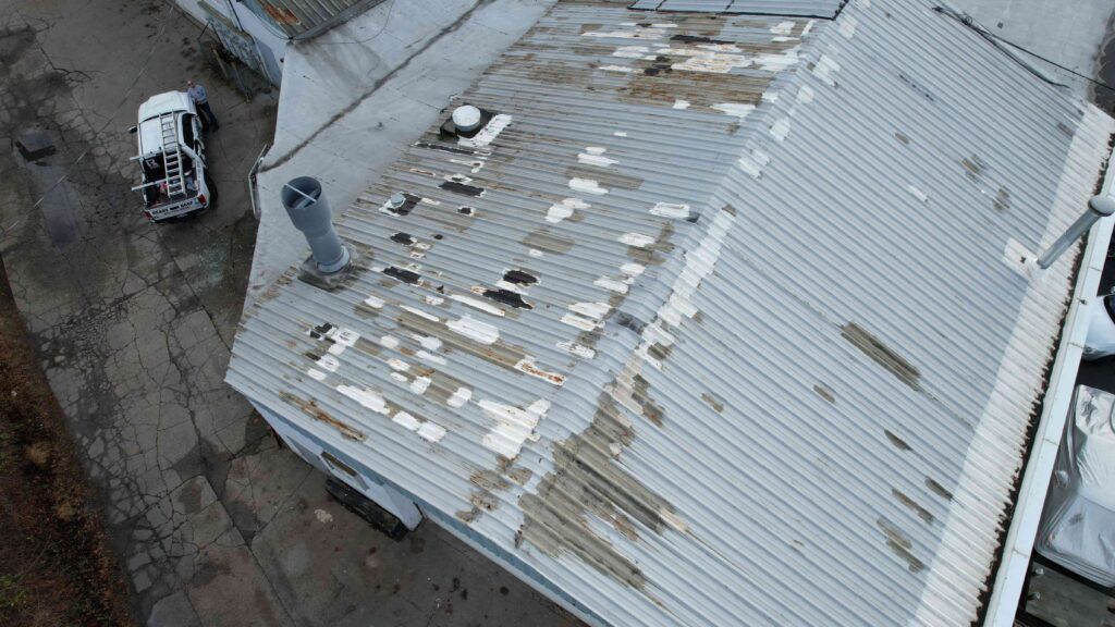 Aerial view of a damaged corrugated metal roof with missing panels and a vehicle beside the building