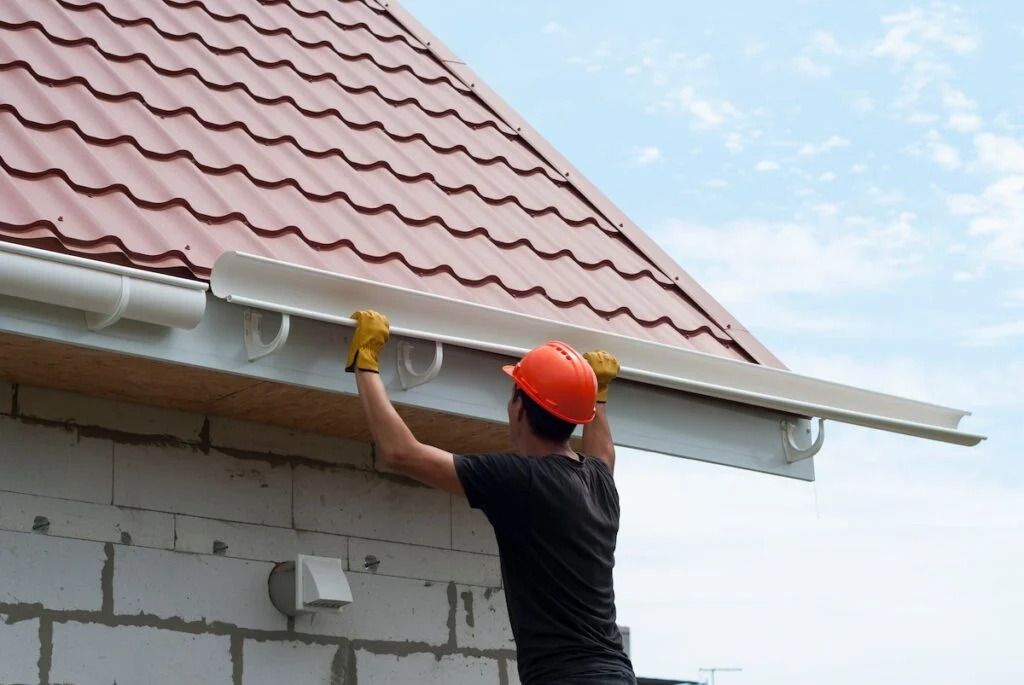 Person wearing an orange hard hat cleaning a house roof with a yellow cloth.
