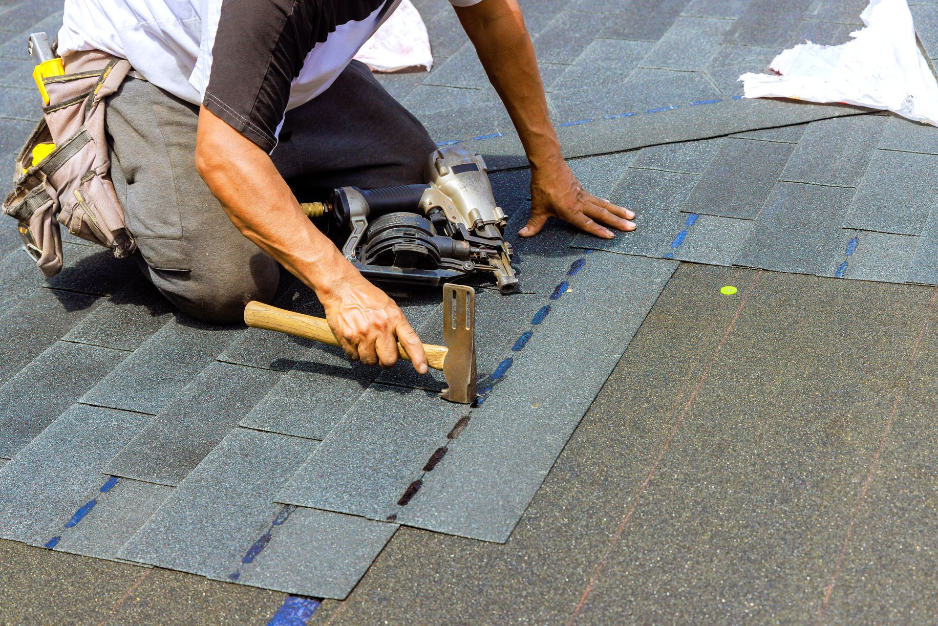 Worker installing asphalt shingles on a roof with a hammer and nails