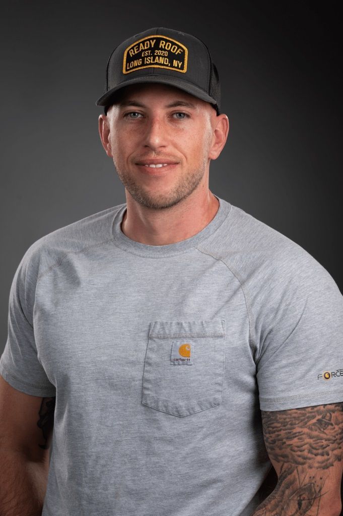 Man in gray T-shirt and black cap posing against a dark background
