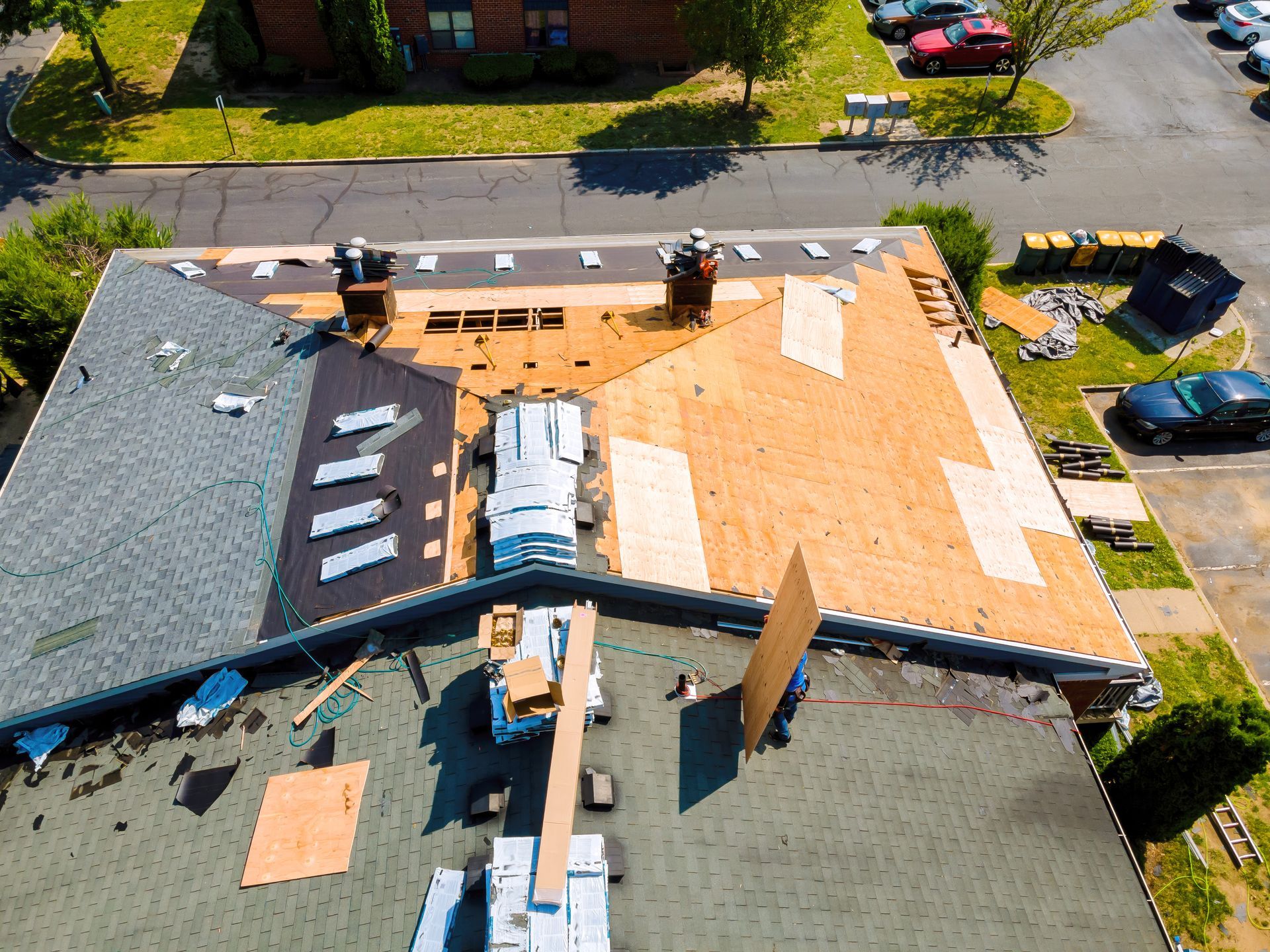 Aerial view of a house roof under repair, with exposed plywood and shingles being replaced.