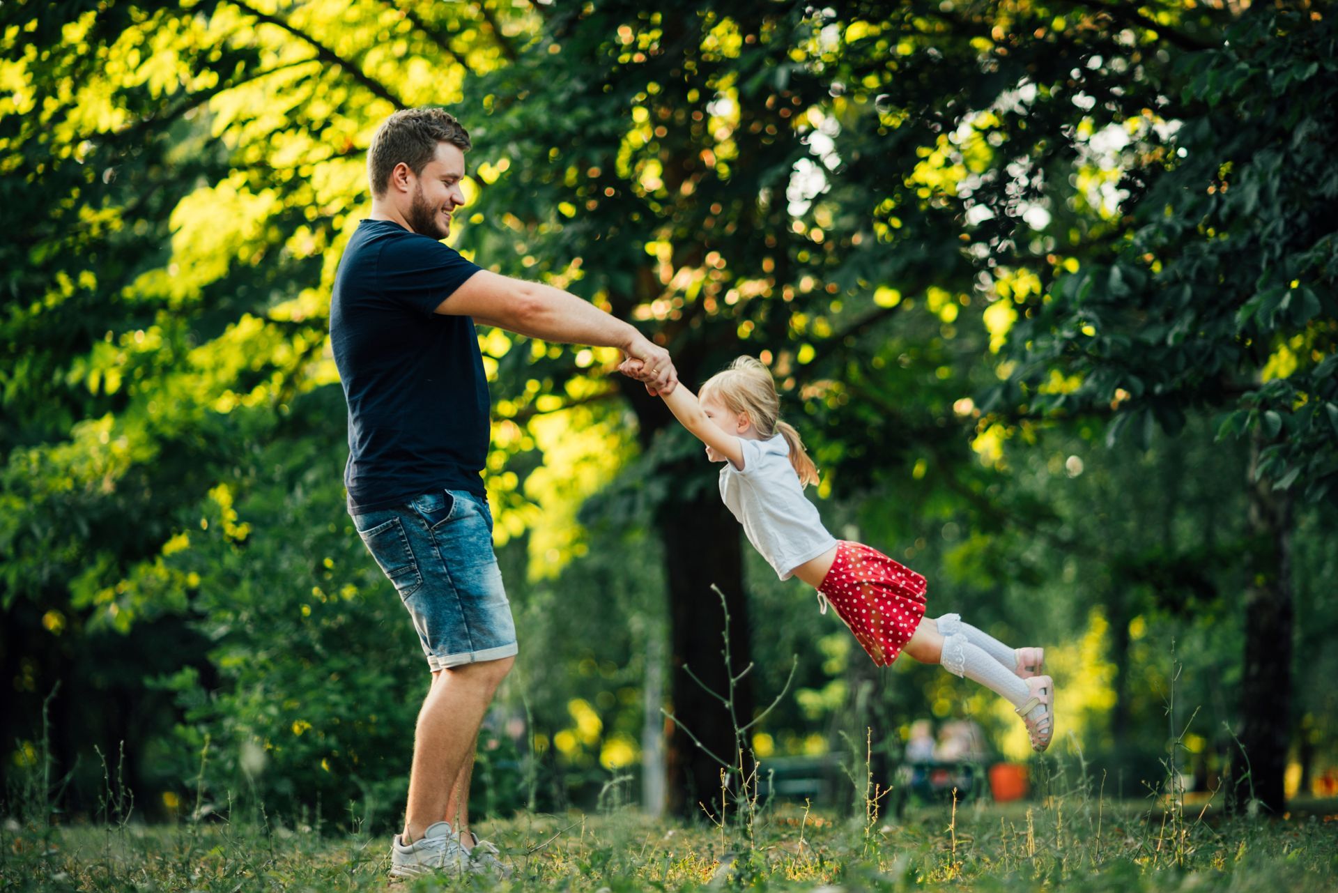a man is holding a little girl 's hand in a park