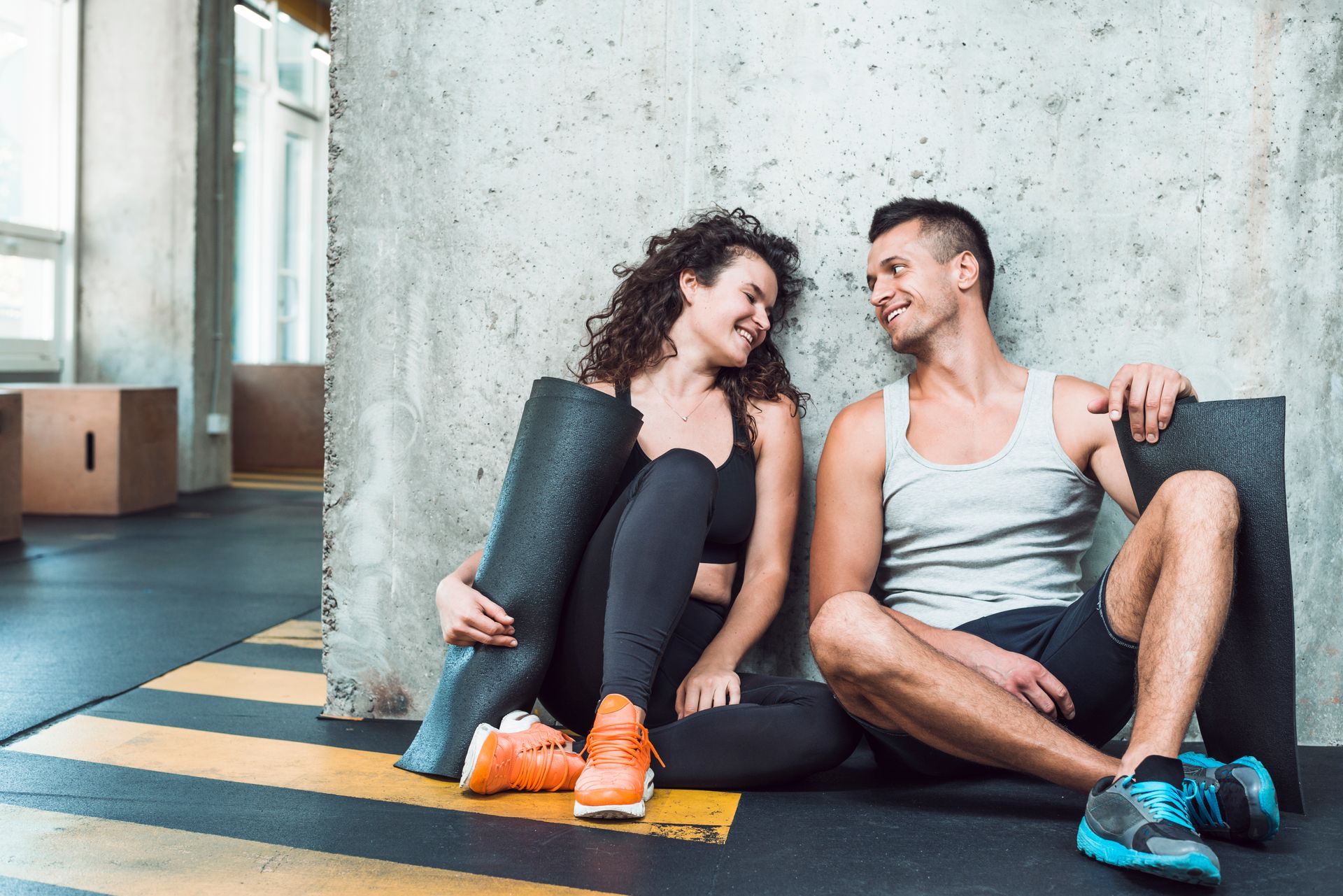 A man and a woman are sitting on the floor in a gym looking at each other.