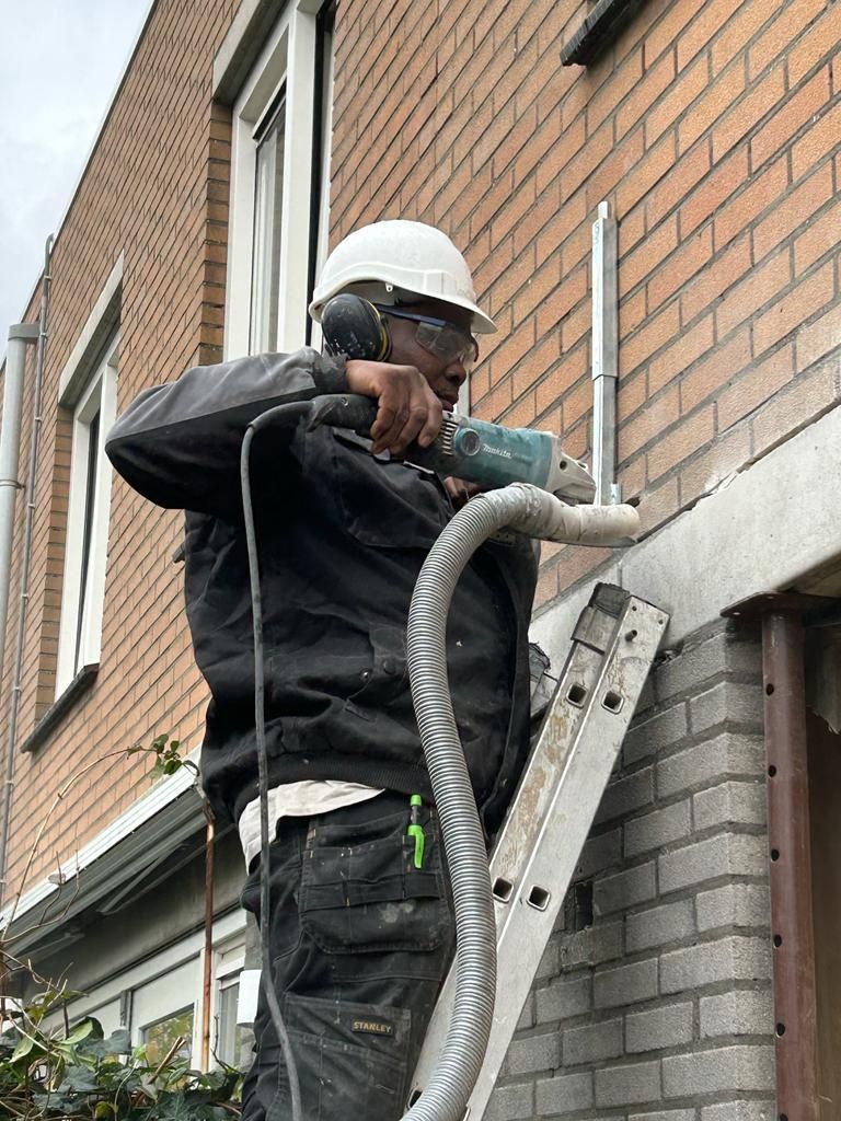 Een man staat op een ladder en gebruikt een slijpmachine op een bakstenen muur.