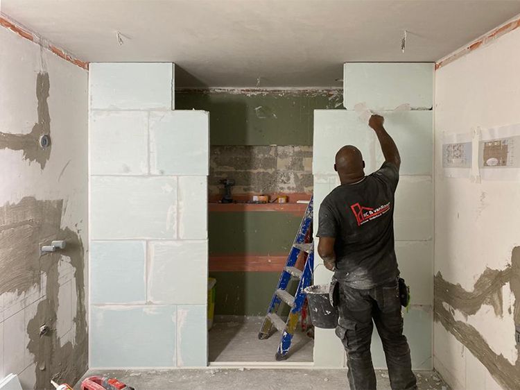 Een man in een zwart shirt staat in een kamer met een ladder.