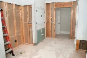 Partially demolished room with exposed studs, drywall patches, and a ladder on the left