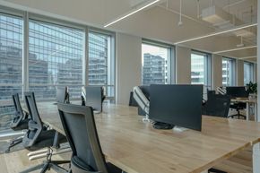 Modern open office with desks, chairs, and large windows overlooking city buildings