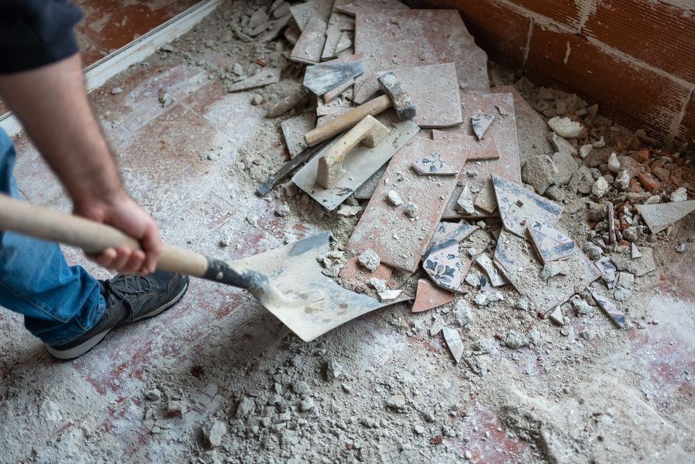 Person shoveling rubble and broken bricks from a damaged floor near brick walls
