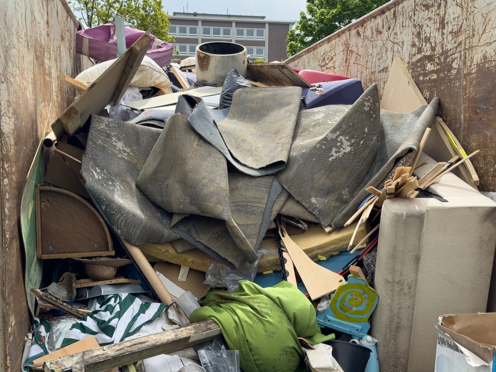Overflowing dumpster filled with broken furniture, wood, and debris in an outdoor alley