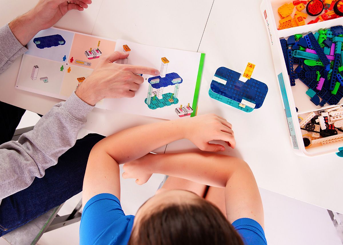 Two children smiling and building a colorful block tower at a table indoors