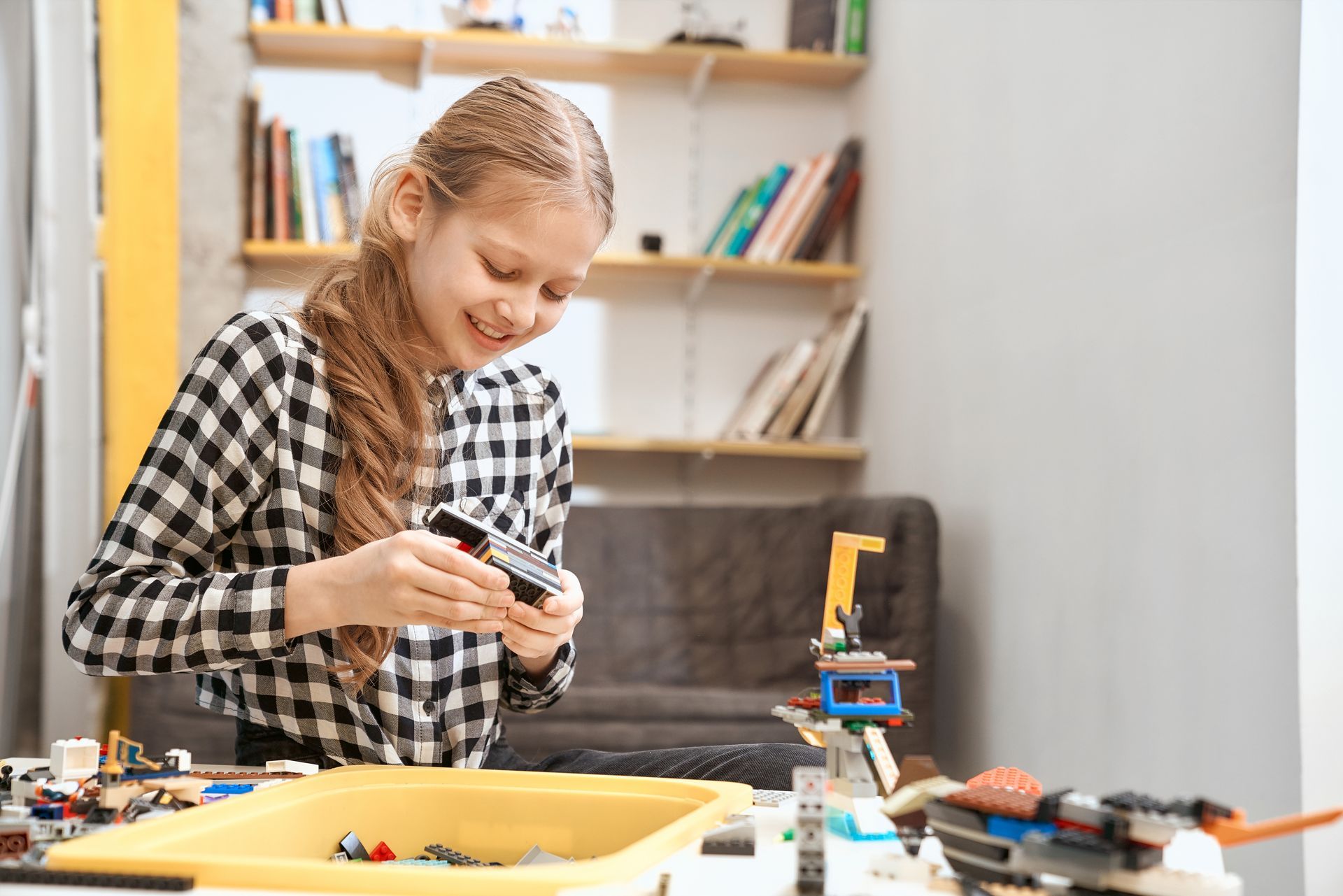 Children and an adult building a colorful LEGO city together at a table, smiling in a bright playroom