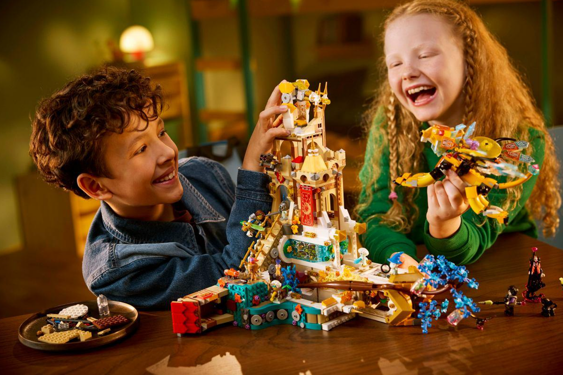 Two children laughing while building a colorful LEGO castle on a table