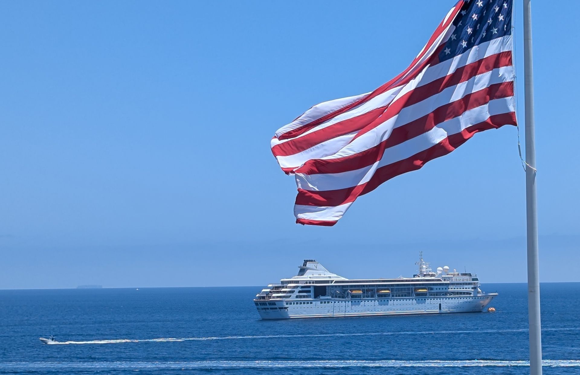 An american flag is flying in front of a cruise ship in the ocean