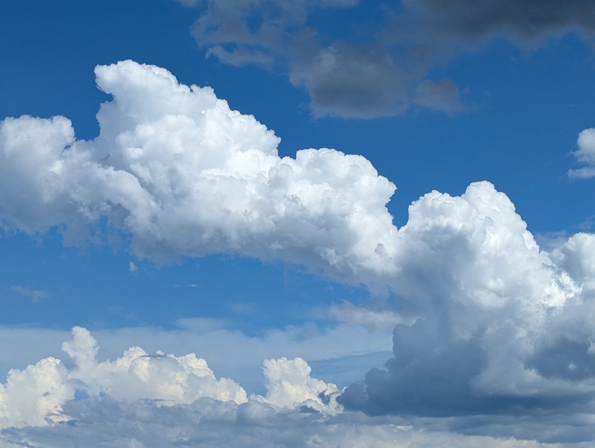 White puffy clouds against a bright blue sky, some hints of gray clouds.