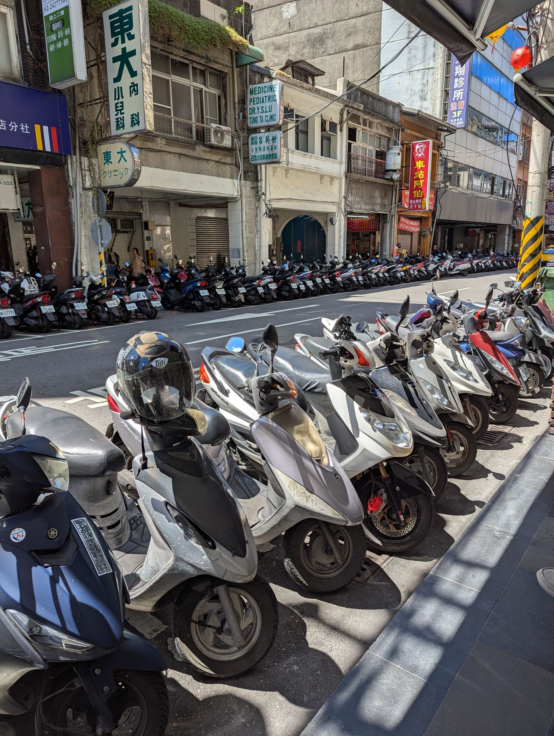 Row of parked scooters on a city street, with buildings and shops in the background.