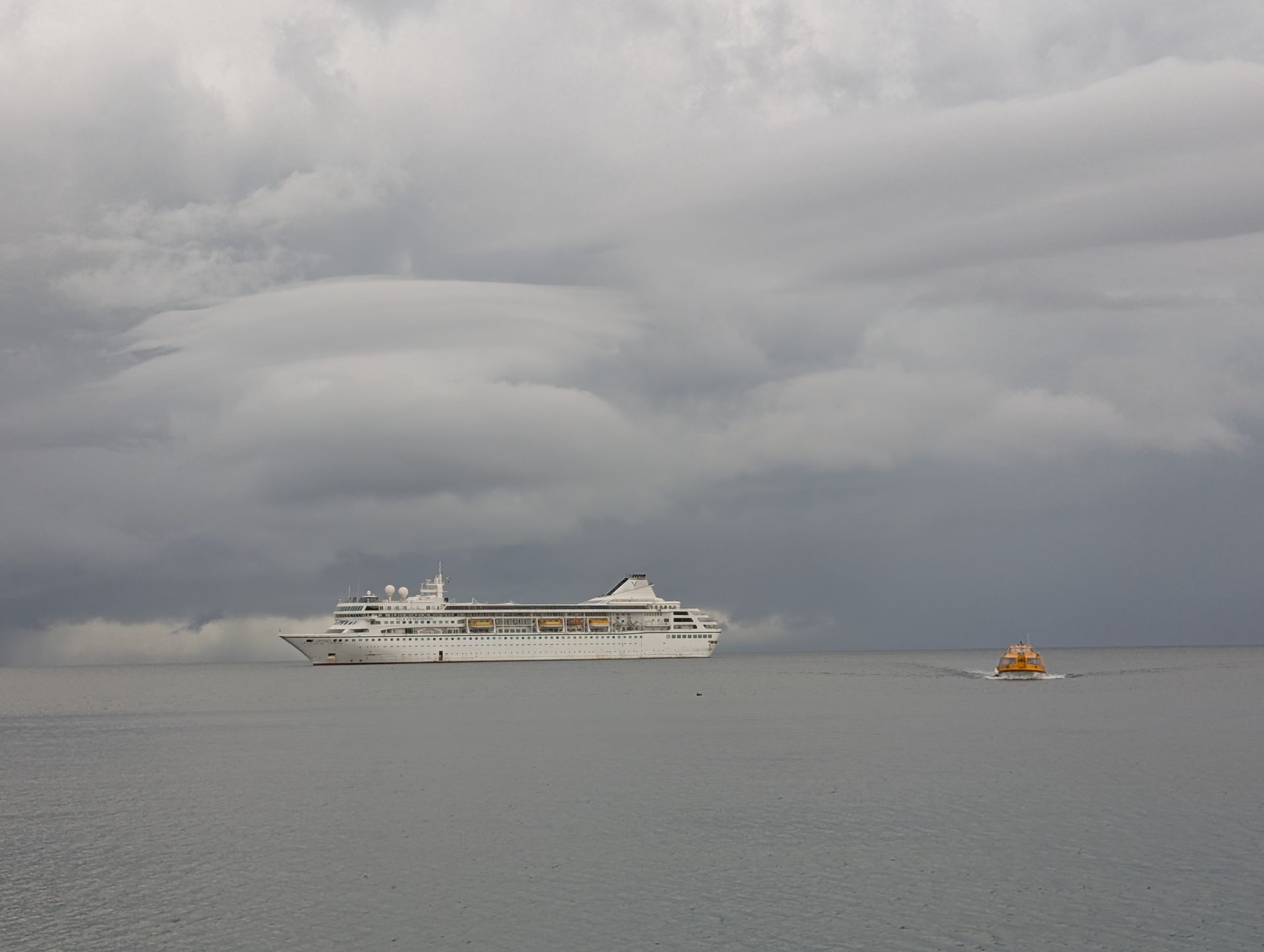 Cruise ship on calm water under a cloudy sky with a small boat nearby.