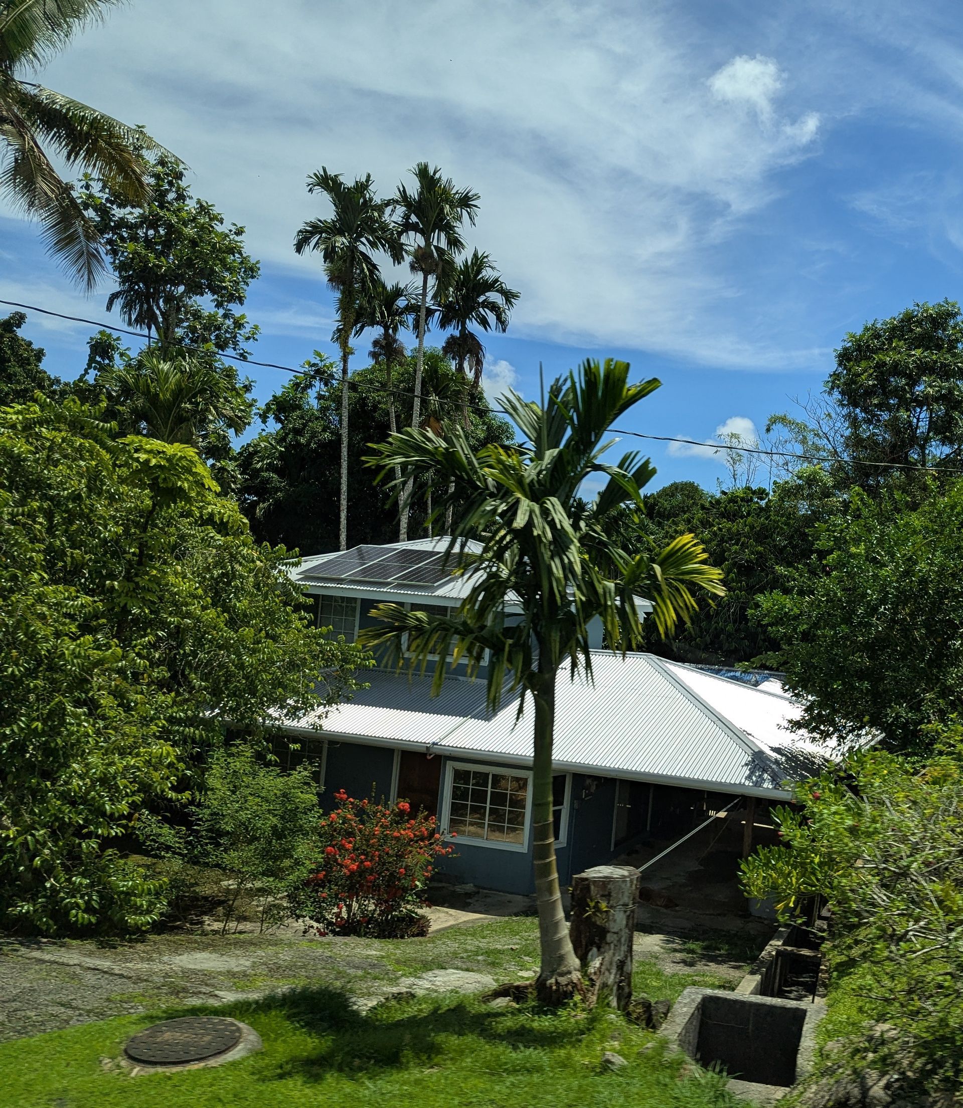 House with white roof, surrounded by green trees under a blue sky.