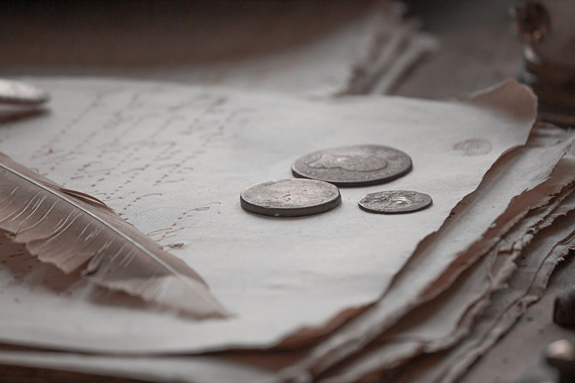 A feather pen is laying on top of a piece of paper with coins on it.