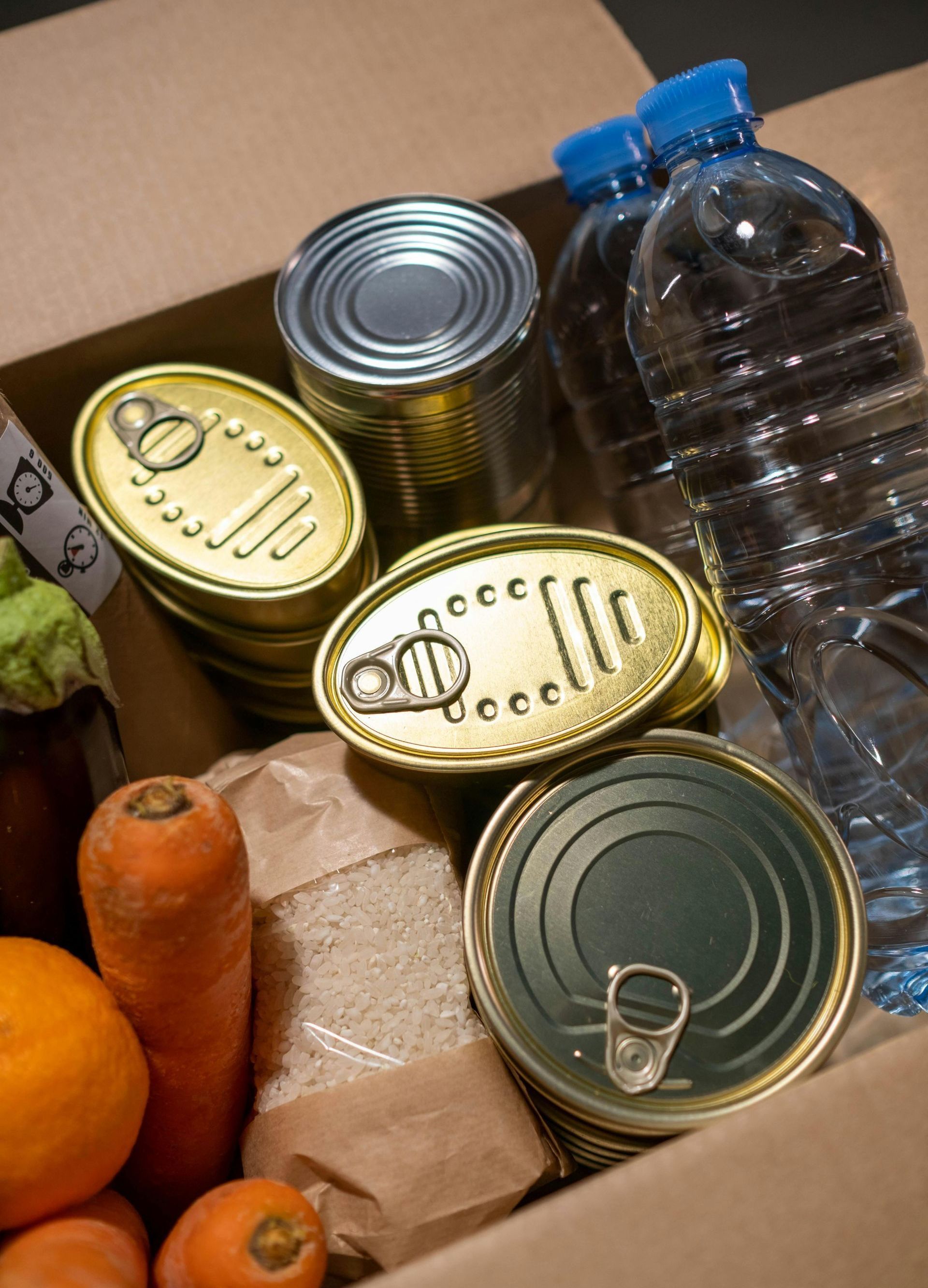 A cardboard box filled with canned food and a bottle of water.