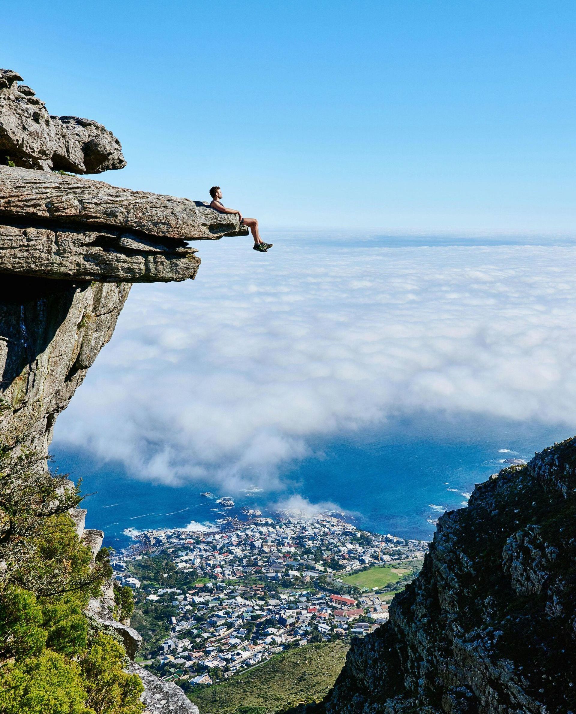 A person is sitting on the edge of a cliff overlooking a city.