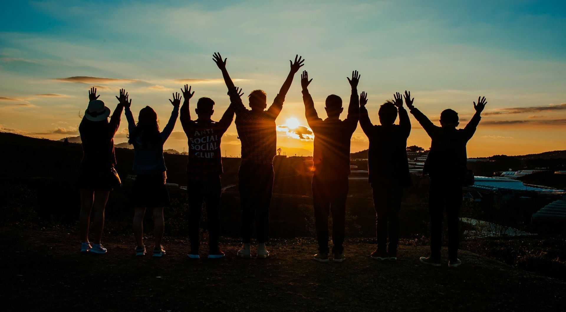 A group of people are standing in a line with their arms in the air at sunset.