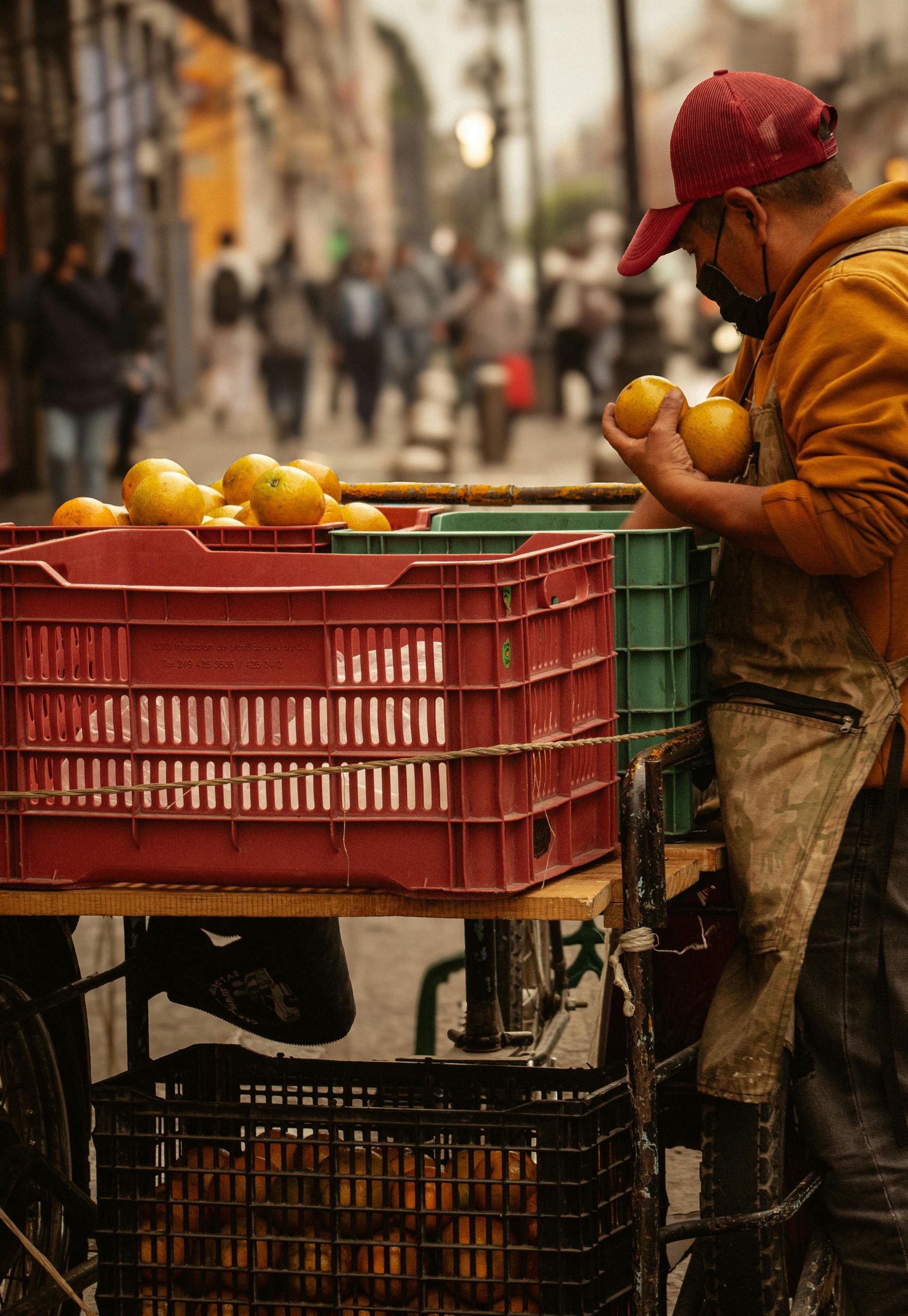 A man is standing next to a cart filled with crates of fruit.
