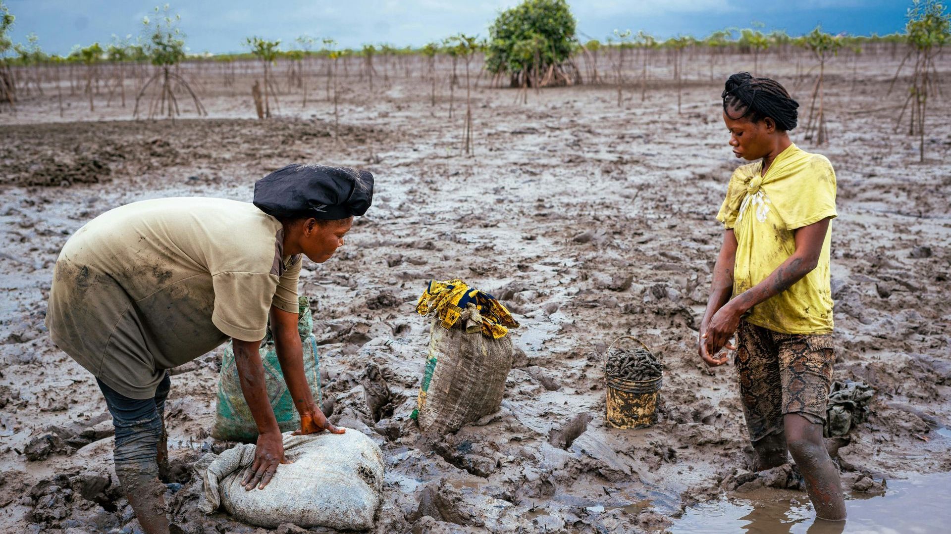 Two women are standing in the mud in a field.