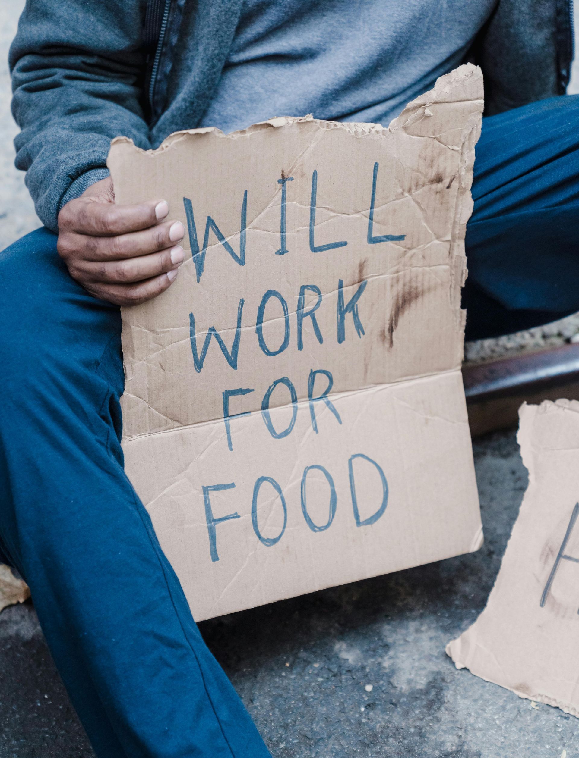 A man is sitting on the ground holding a cardboard sign that says `` will work for food ''.
