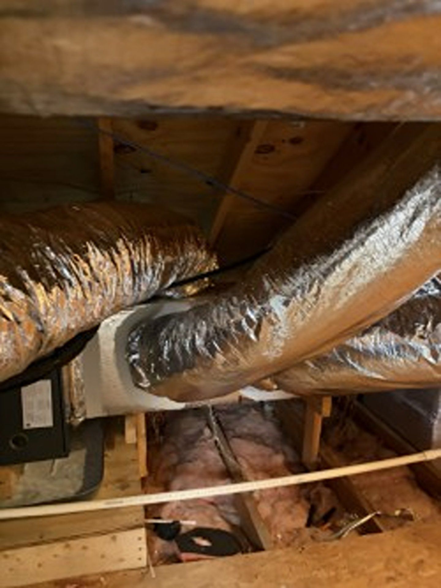 Insulated HVAC ducts and wooden joists in an attic crawlspace