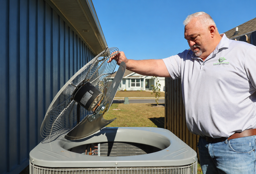 Man lifting an open air conditioner lid beside a blue building on a sunny day