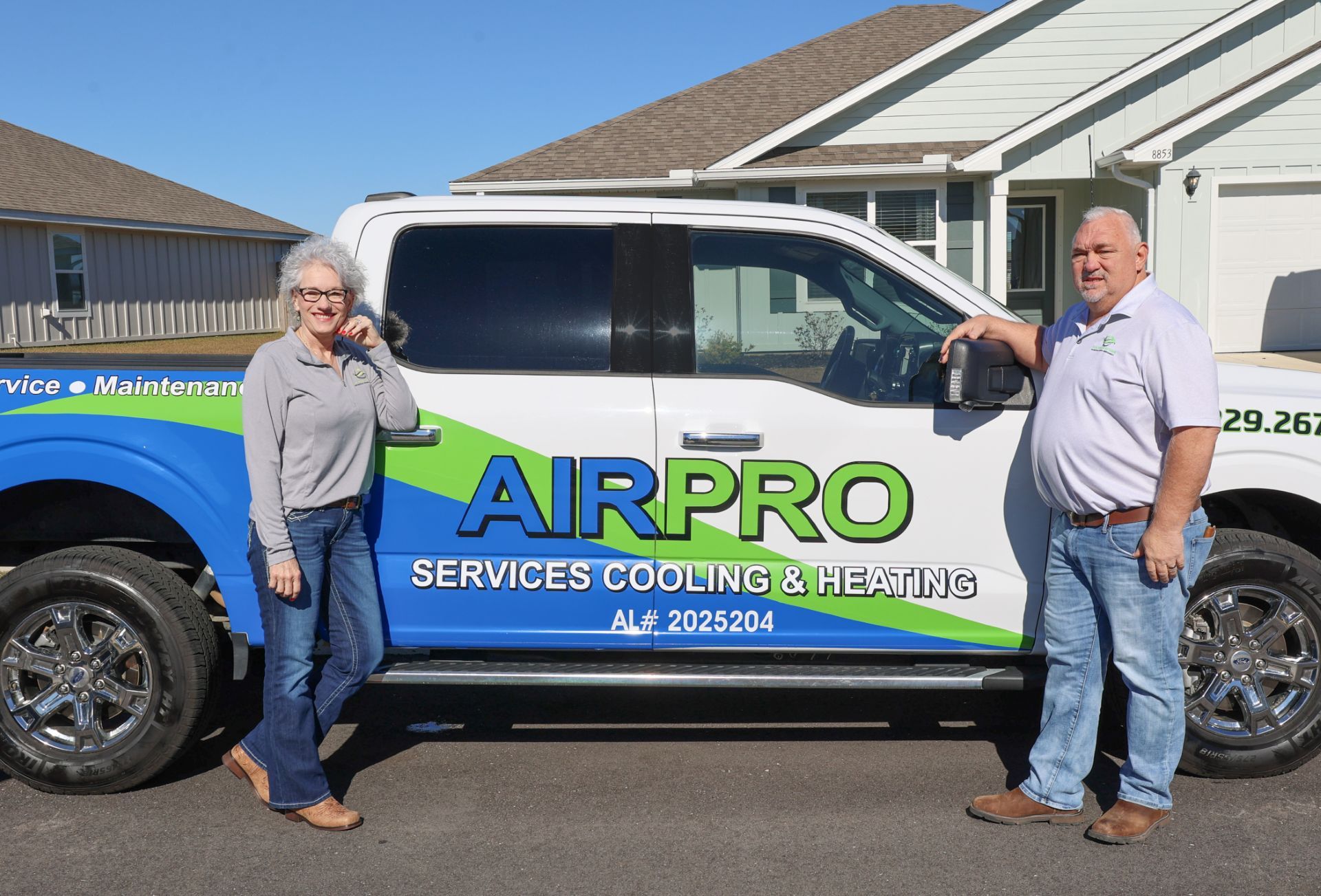 Two people standing beside a blue-and-white AIRPRO service van in a suburban driveway.