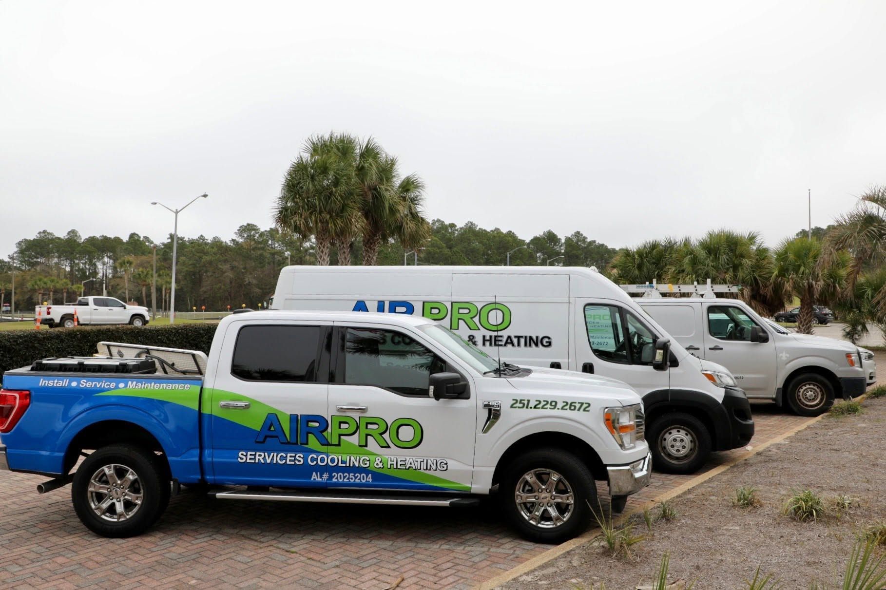 Two AIRPRO service trucks parked outdoors near palm trees and a gravel lot