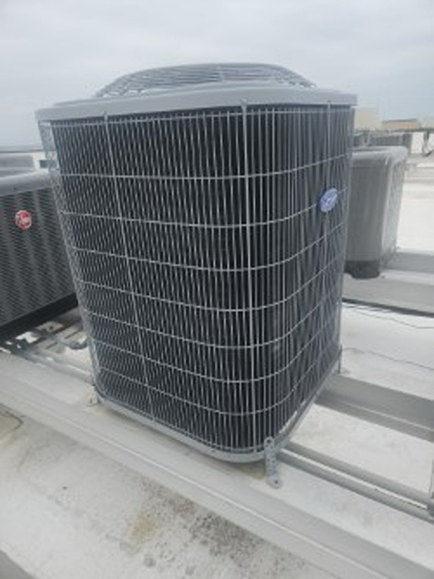 Outdoor rooftop HVAC condenser unit with black grille on a white rooftop under cloudy skies