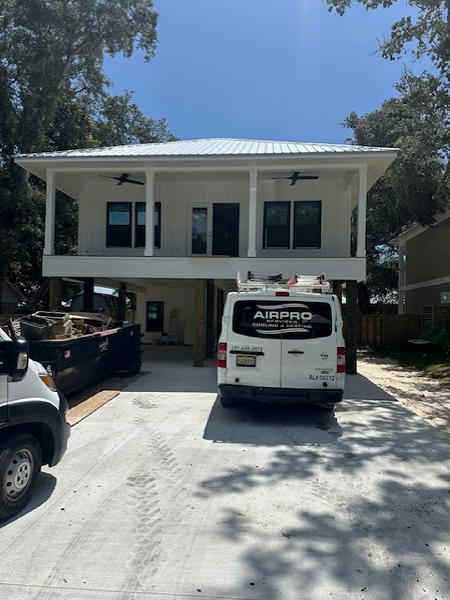 Two-story white house with parked moving truck and vehicle in the driveway under a bright blue sky
