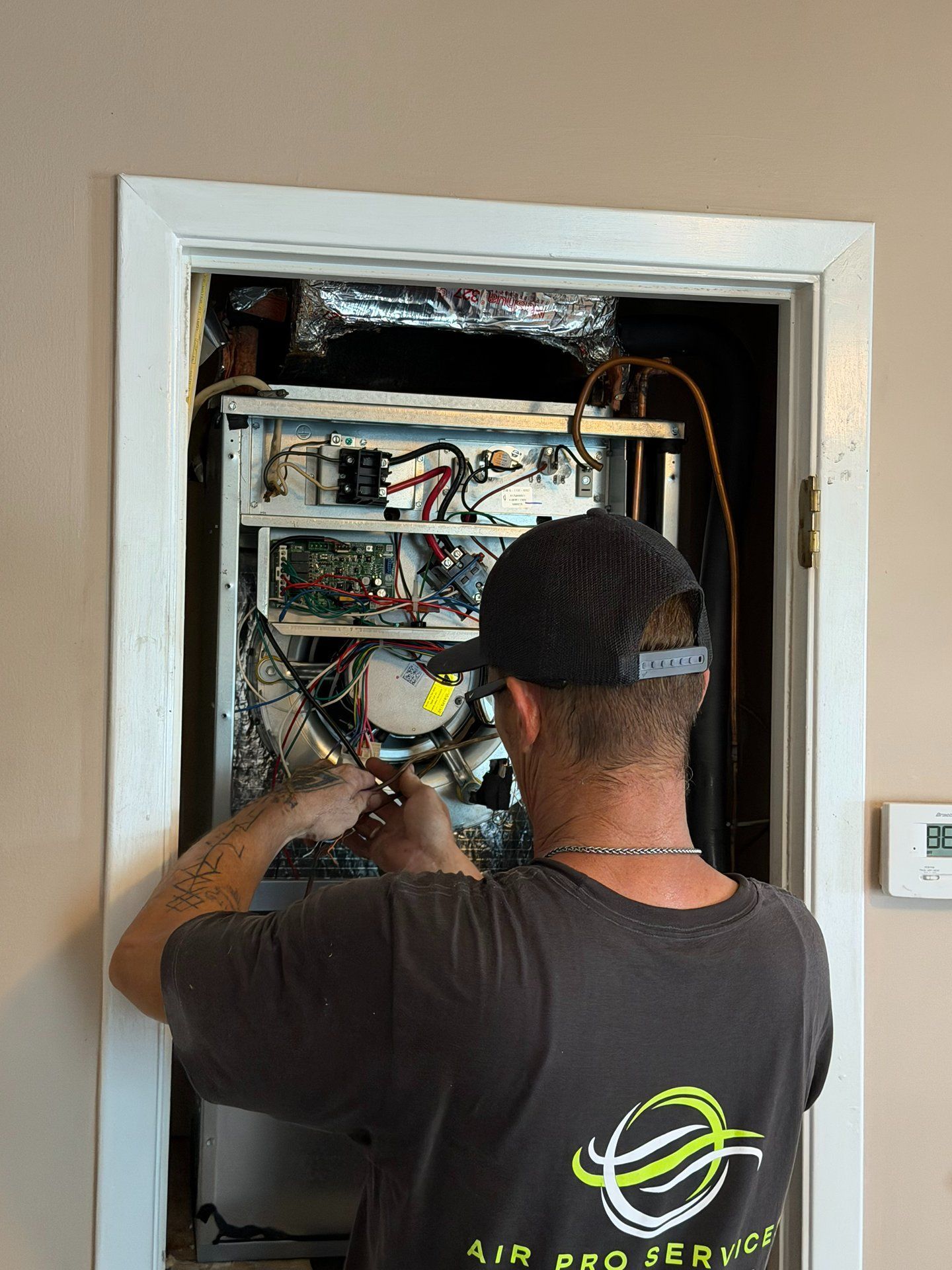 Technician working inside an open wall panel with exposed electrical wiring and equipment.