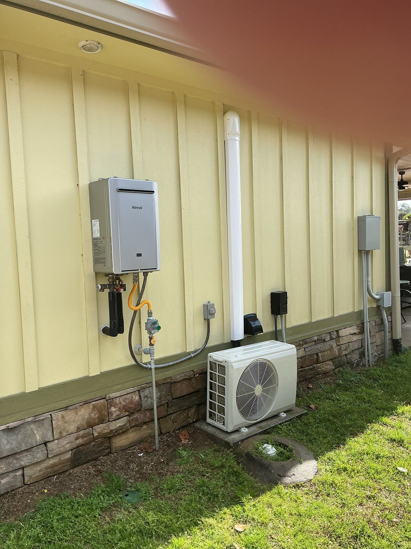 Exterior wall with electrical boxes, conduit, and a white AC unit beside a yellow house.