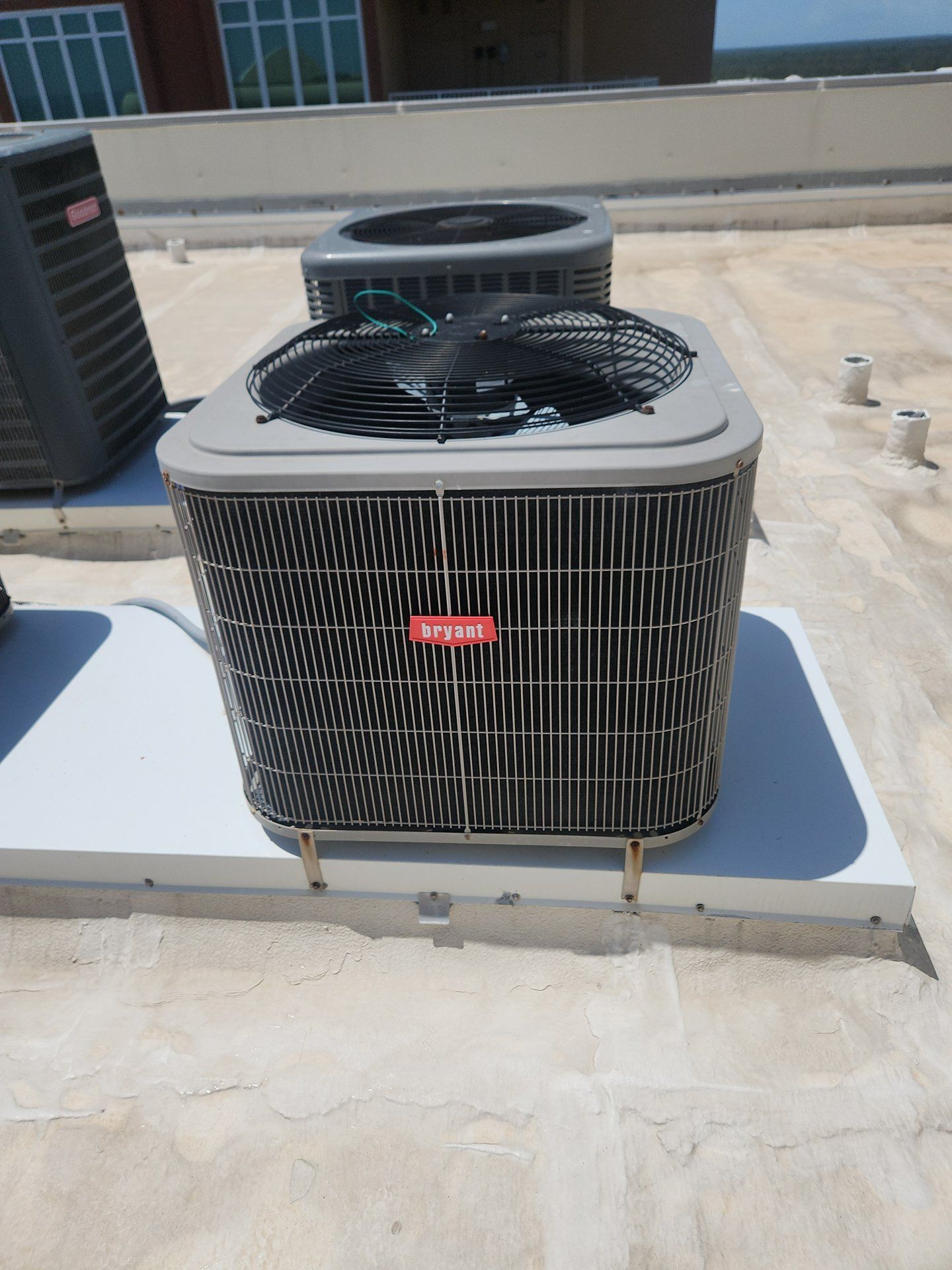 Rooftop air conditioner condenser unit with black fan and red logo on a white base.