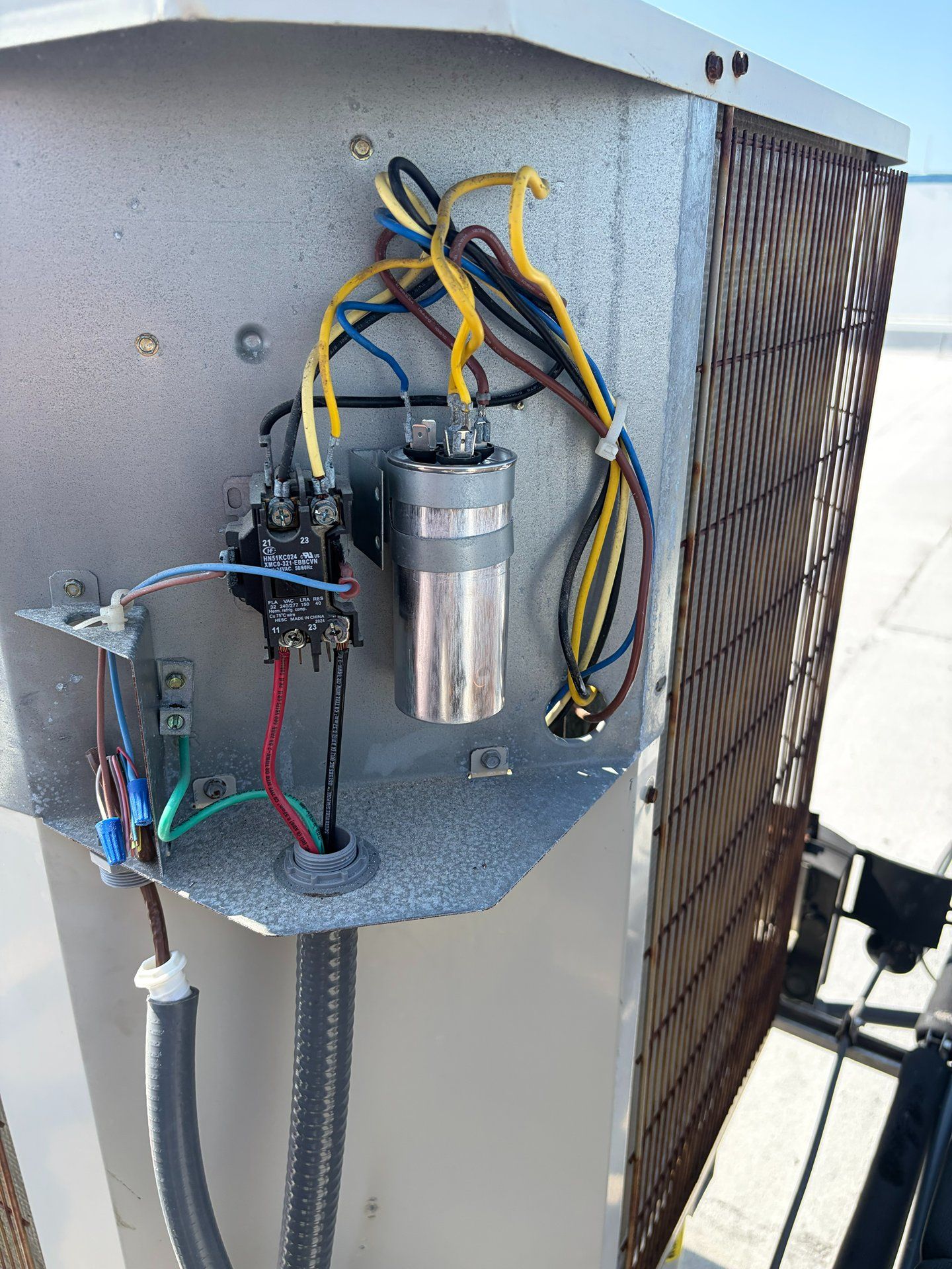 Electrical components and wiring inside an outdoor HVAC unit, with a visible coil on the right.