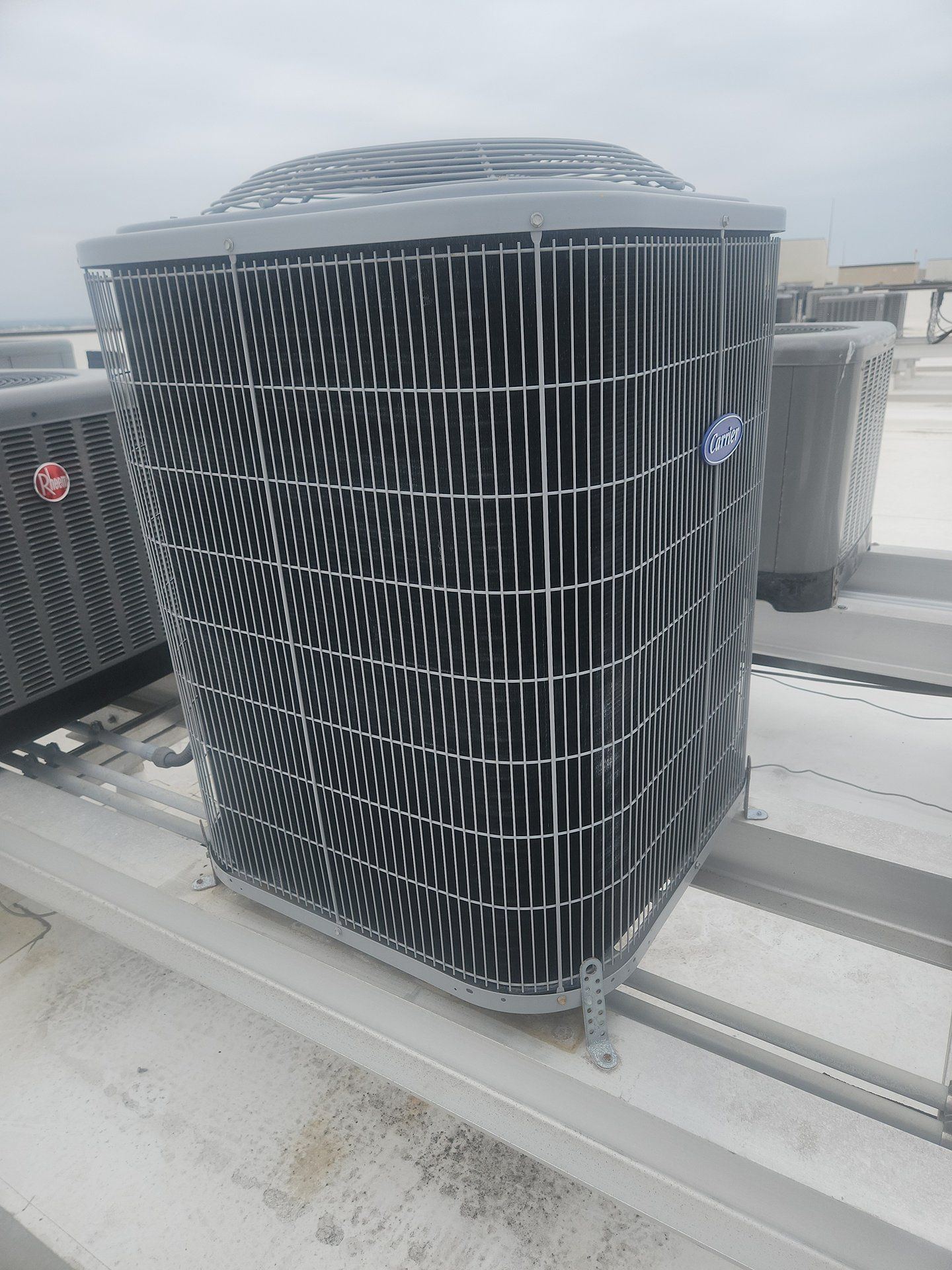 Outdoor HVAC unit with black grille on a flat rooftop, surrounded by other rooftop equipment.