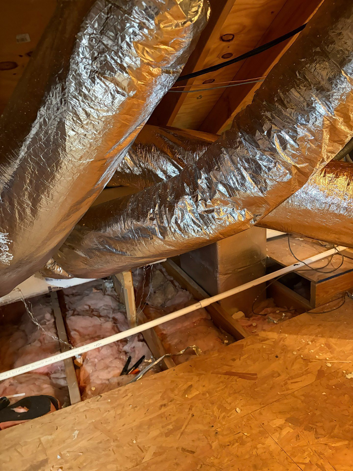 Attic with silver insulated ductwork, wooden framing, and exposed insulation on the floor