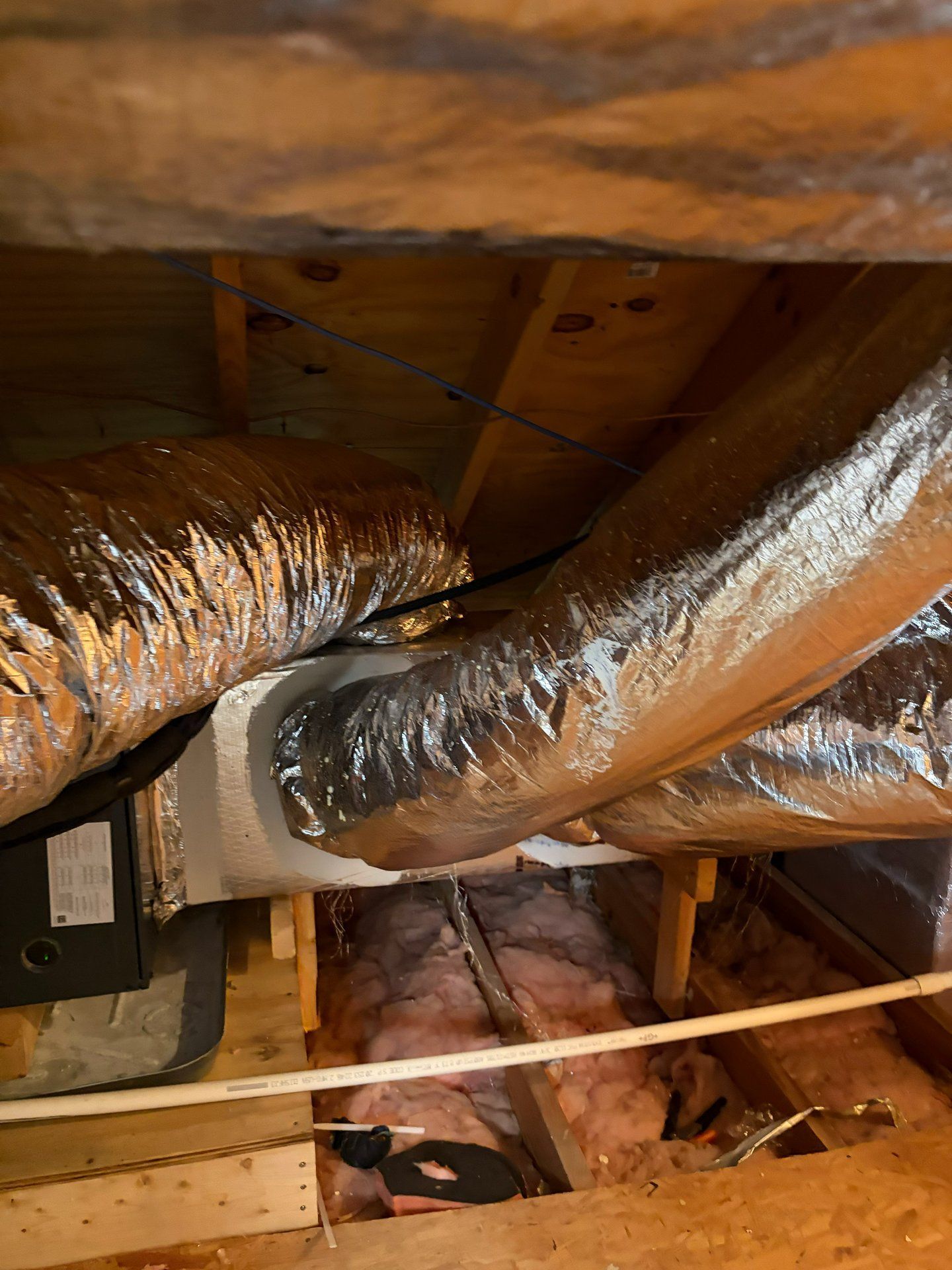 Attic with large insulated HVAC ducts and exposed wooden beams over pink insulation