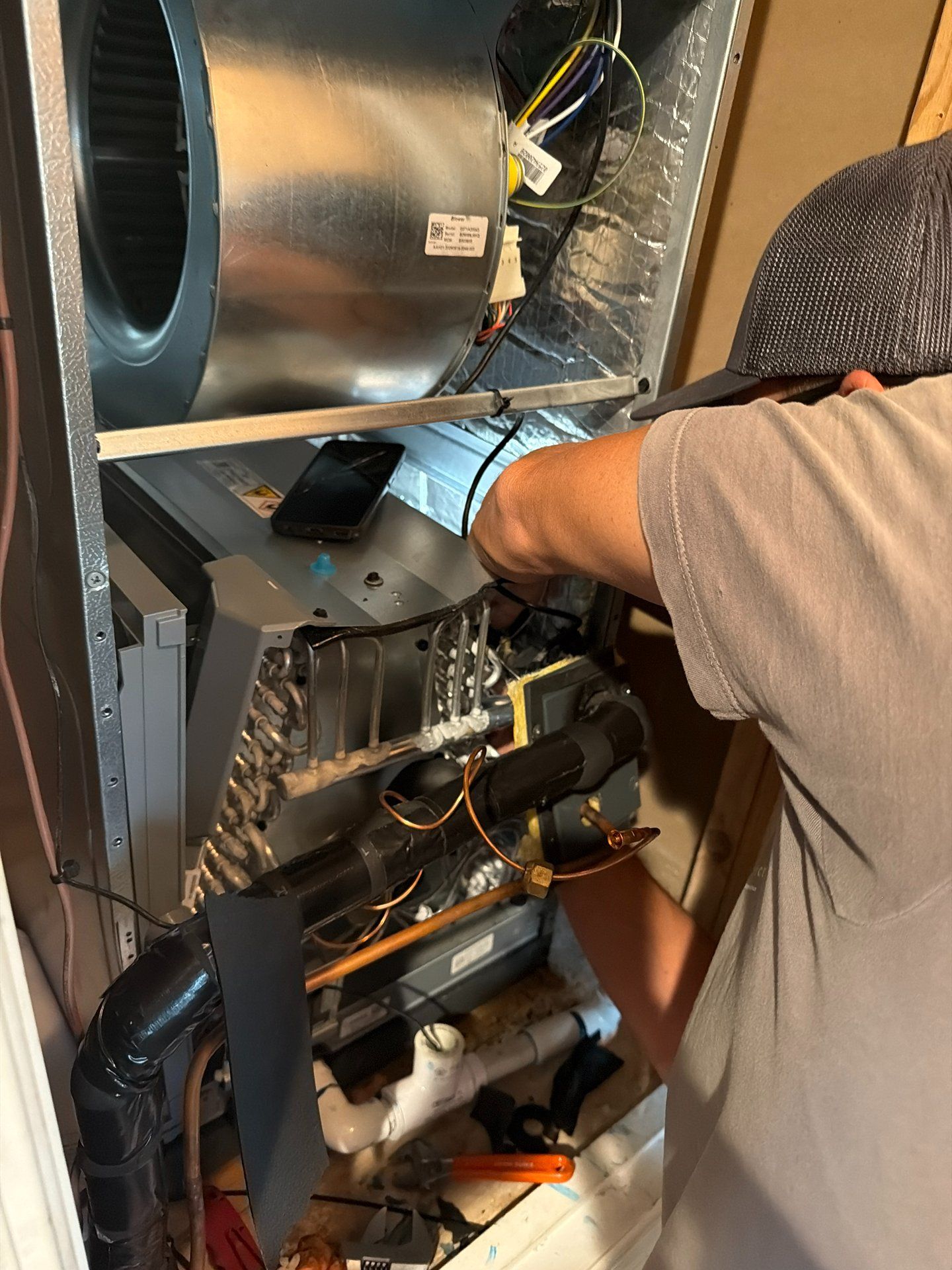 Technician repairing HVAC unit inside an open metal cabinet, with wiring and ductwork visible.